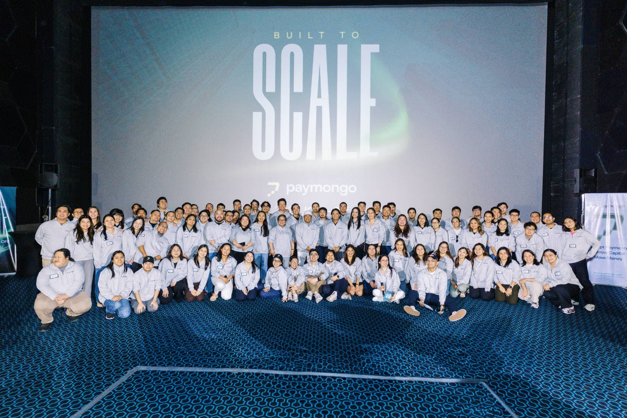 The PayMongo team gathered in front of a Built to Scale screen at a company event