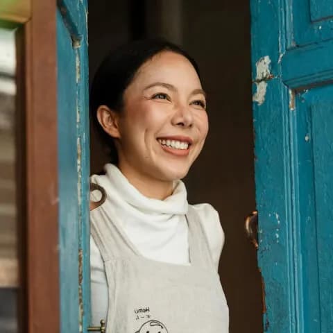 A woman is smiling while looking out of a blue door.