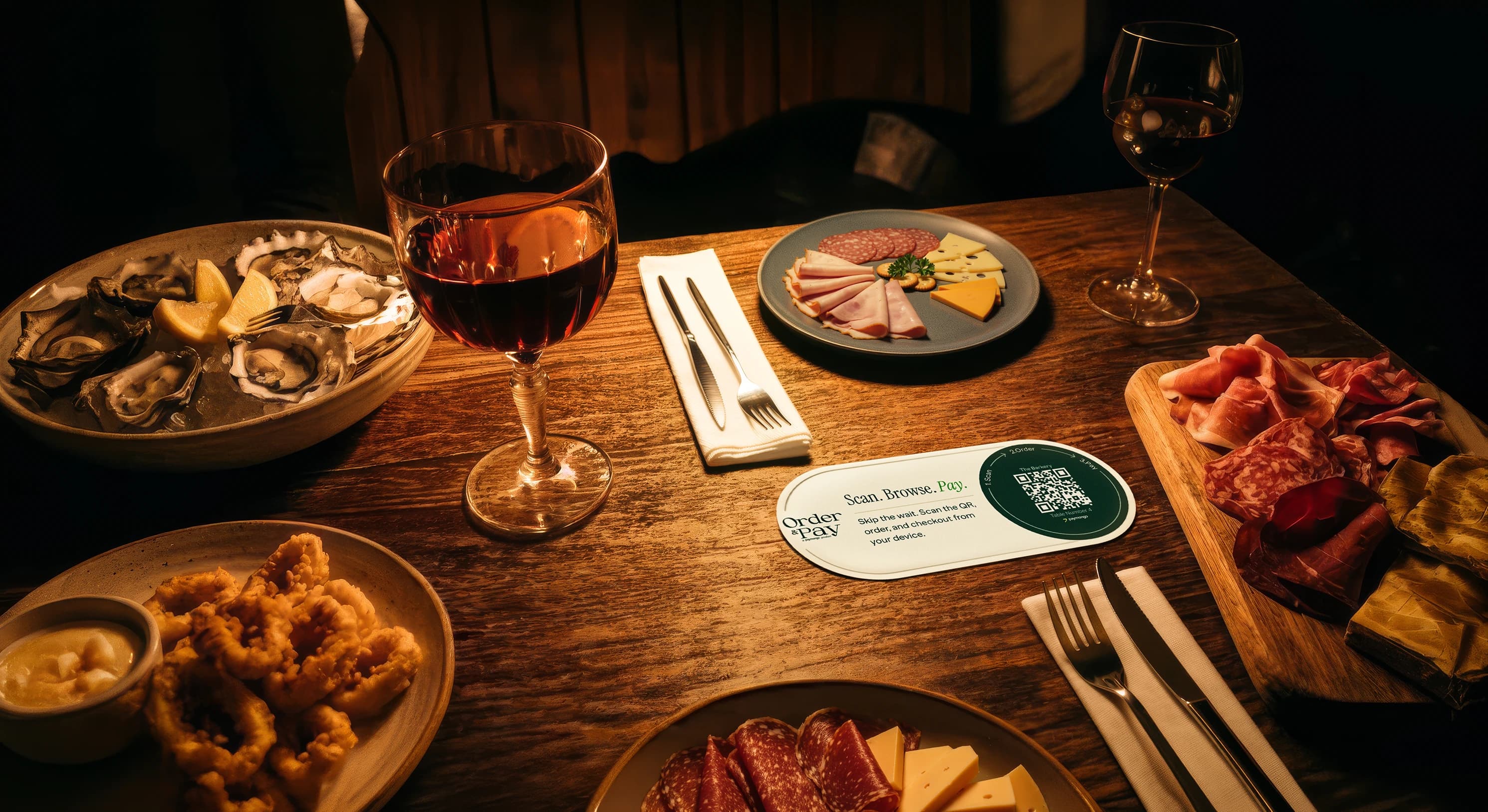 An Order and Pay QR code card on a restaurant table, beside a wine glass and a charcuterie board — diners scan it to open the menu, order, and pay from their own phone