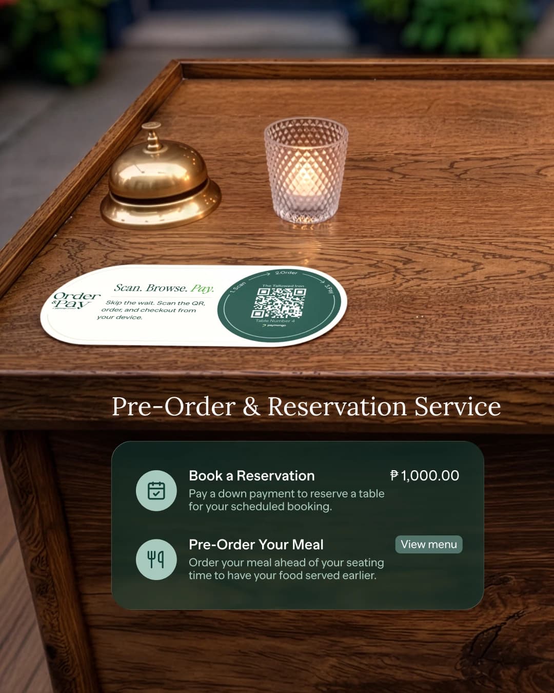 An Order and Pay QR card on a restaurant host stand beside a brass service bell, with two payable items shown over it — Book a Reservation and Pre-Order Your Meal