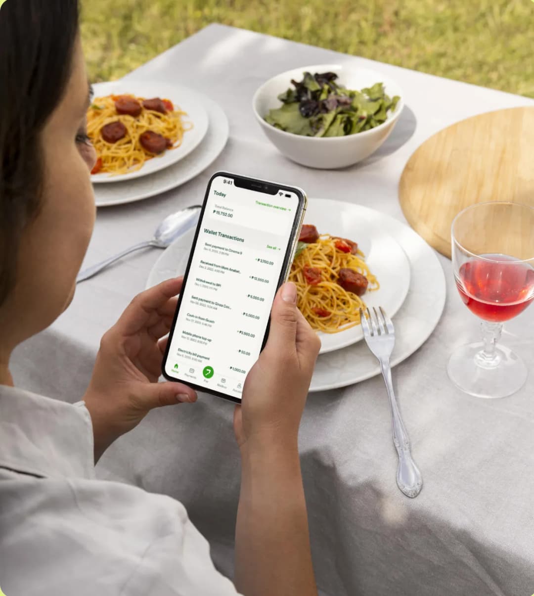 A woman sitting at a table with a plate of spaghetti and a glass of wine